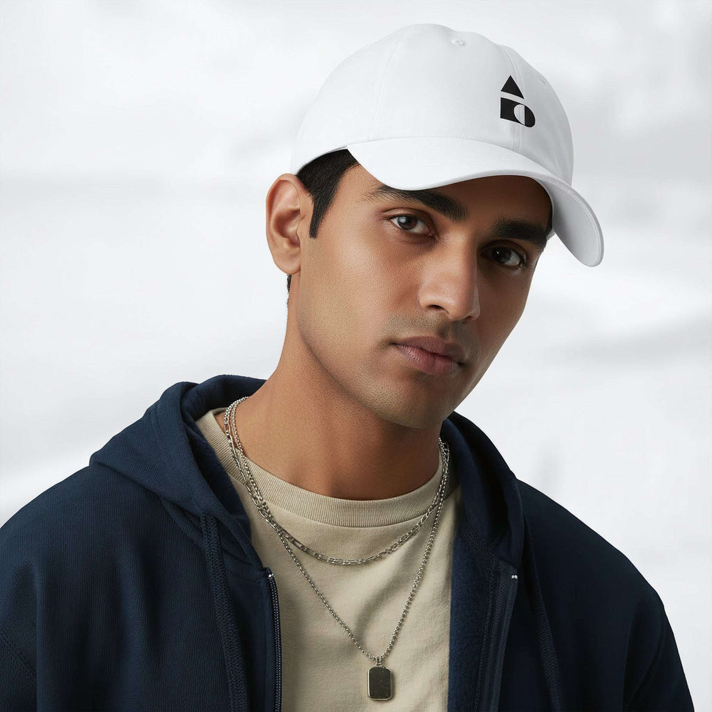 Male model wearing the white Under Armour x Form Fundamentals Stamp Cap (No.03) in a three‑quarter front pose; the cap’s curved brim and black Form Fundamentals logo are visible, styled with a navy hoodie over a beige top and layered chain in a neutral studio setting.