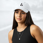 Female model wearing the white Under Armour x Form Fundamentals Stamp Cap (No.03); front view of the cap with black geometric emblem and curved brim, paired with a black tank top and layered necklaces against a softly blurred background.
