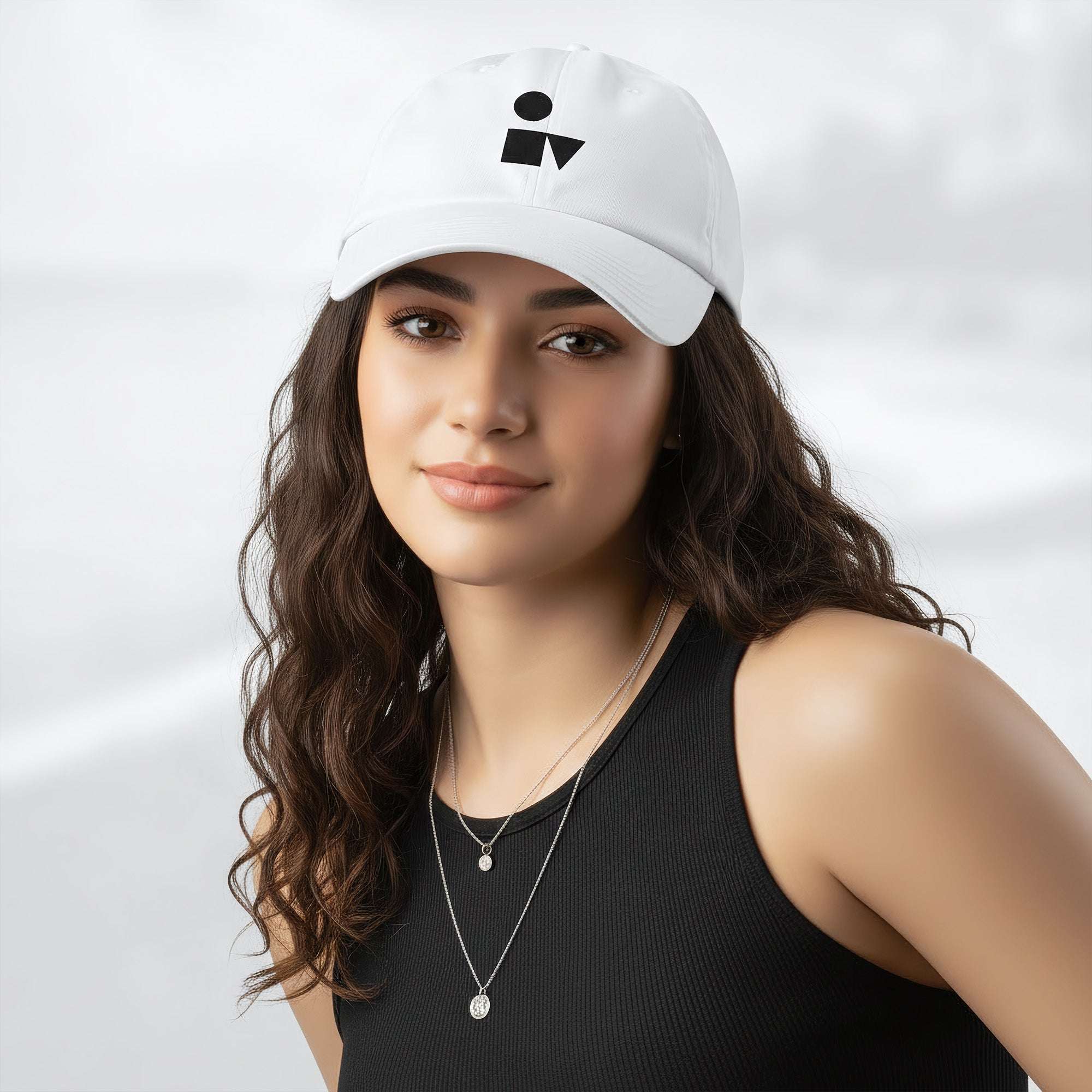 Female model wearing the white Under Armour x Form Fundamentals Stamp Cap (No.05); front view of the cap with black geometric emblem and curved brim, paired with a black tank top and layered necklaces against a softly blurred background.