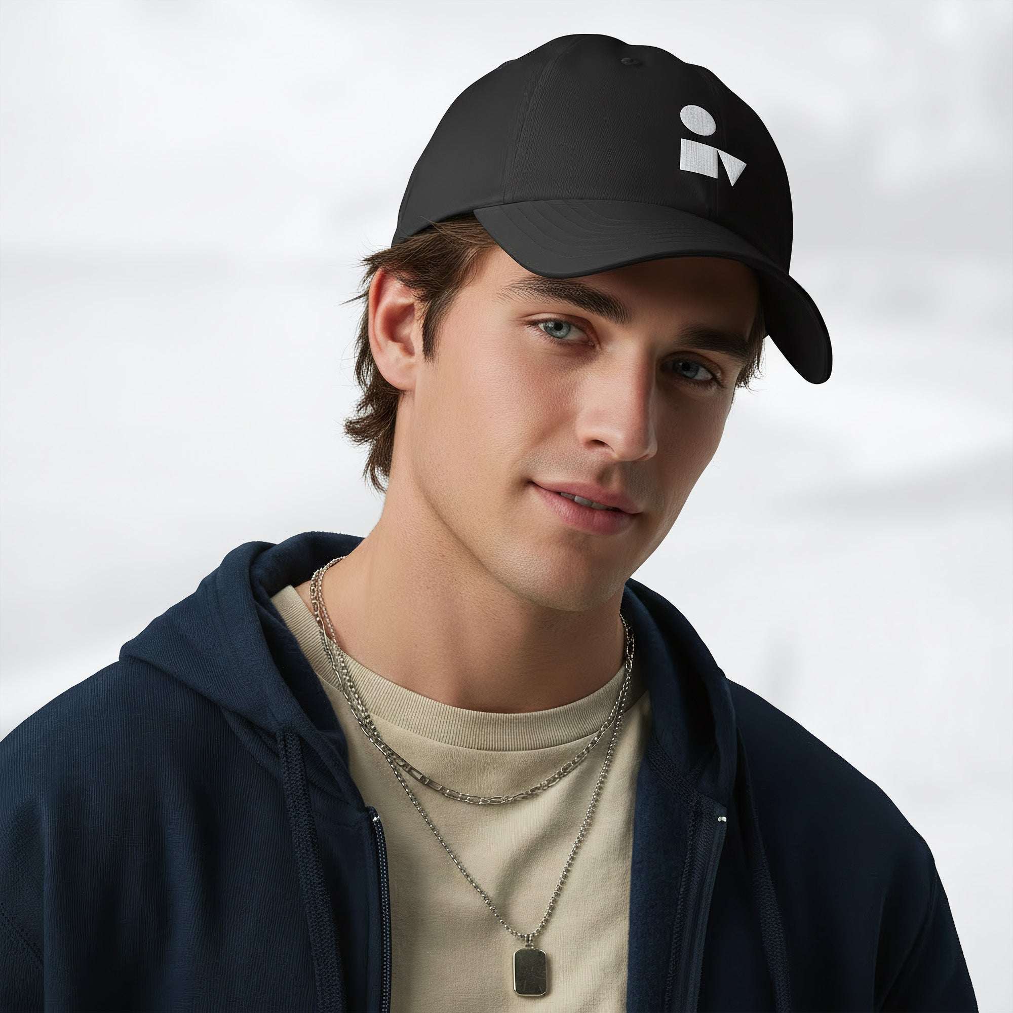 Male model wearing the black Under Armour x Form Fundamentals Stamp Cap (No.06) in a three‑quarter front pose; the cap’s curved brim and white Form Fundamentals logo are visible, styled with a navy hoodie over a beige top and layered chain in a neutral studio setting.