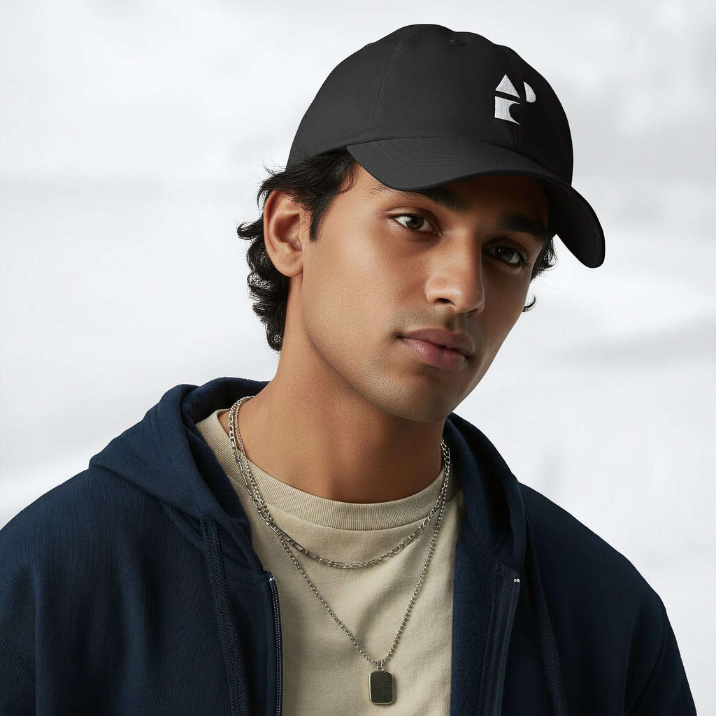 Male model wearing the black Under Armour x Form Fundamentals Stamp Cap (No.08) in a three‑quarter front pose; the cap’s curved brim and white Form Fundamentals logo are visible, styled with a navy hoodie over a beige top and layered chain in a neutral studio setting.