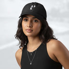 Female model wearing the black Under Armour x Form Fundamentals Stamp Cap (No.08); front view of the cap with white geometric emblem and curved brim, paired with a black tank top and layered necklaces against a softly blurred background.