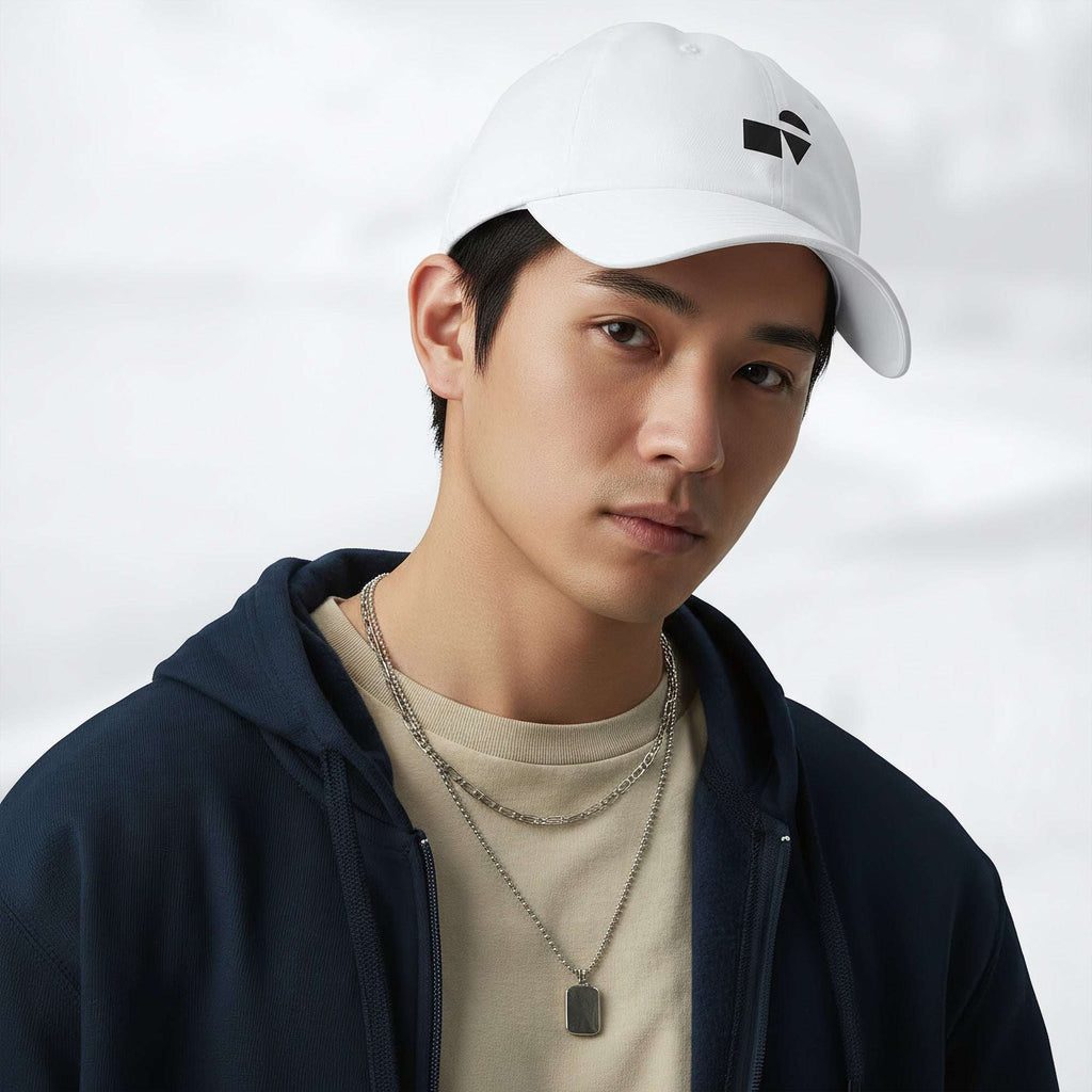 Male model wearing the white Under Armour x Form Fundamentals Stamp Cap (No.09) in a three‑quarter front pose; the cap’s curved brim and black Form Fundamentals logo are visible, styled with a navy hoodie over a beige top and layered chain in a neutral studio setting.