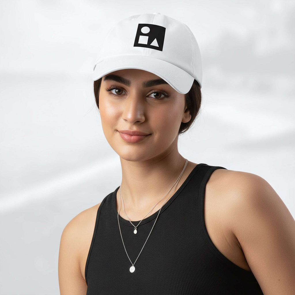 Female model wearing the white Under Armour x Form Fundamentals Stamp Cap (No.13); front view of the cap with black geometric emblem and curved brim, paired with a black tank top and layered necklaces against a softly blurred background.