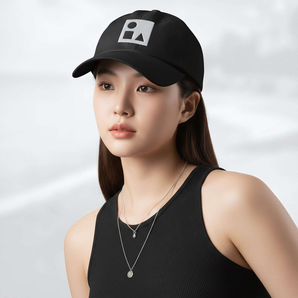Female model wearing the black Under Armour x Form Fundamentals Stamp Cap (No.14); front view of the cap with white geometric emblem and curved brim, paired with a black tank top and layered necklaces against a softly blurred background.