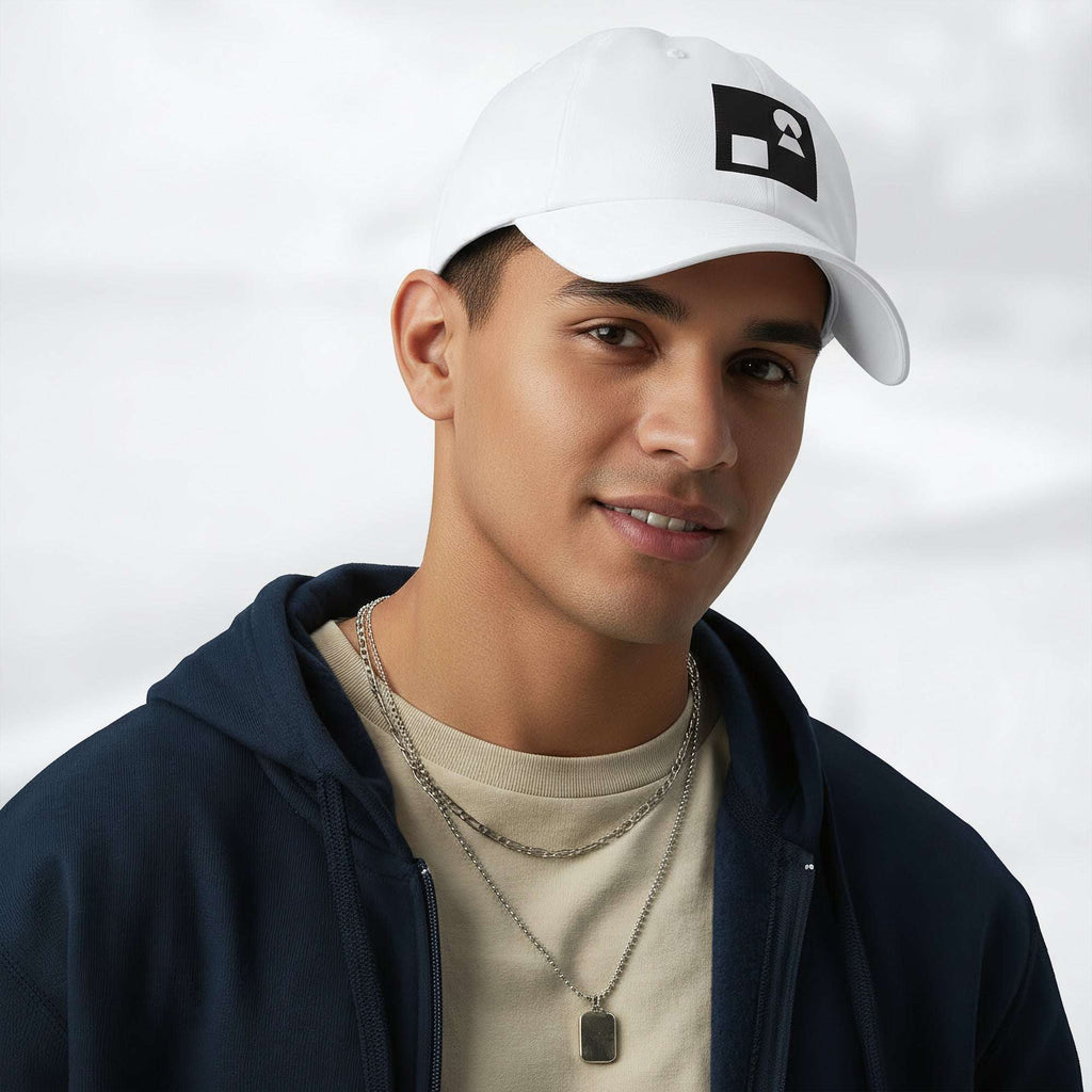 Male model wearing the white Under Armour x Form Fundamentals Stamp Cap (No.15) in a three‑quarter front pose; the cap’s curved brim and black Form Fundamentals logo are visible, styled with a navy hoodie over a beige top and layered chain in a neutral studio setting.