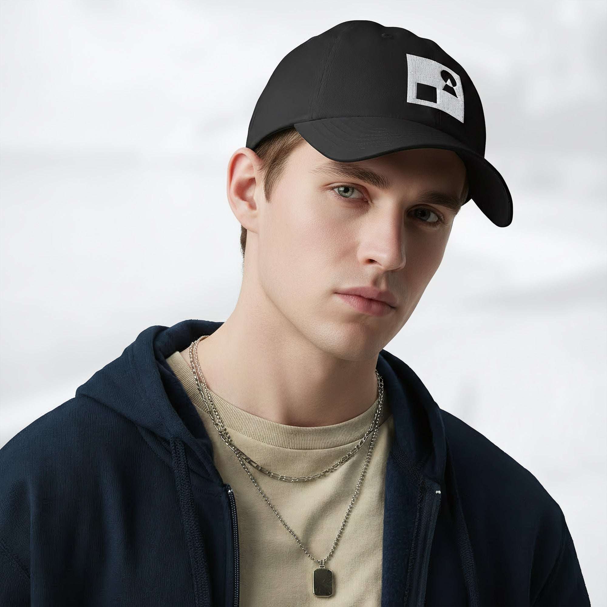 Male model wearing the black Under Armour x Form Fundamentals Stamp Cap (No.16) in a three‑quarter front pose; the cap’s curved brim and white Form Fundamentals logo are visible, styled with a navy hoodie over a beige top and layered chain in a neutral studio setting.