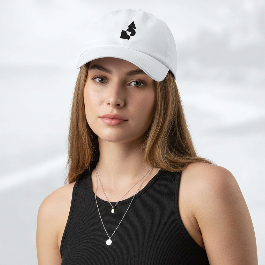 Female model wearing the white Under Armour x Form Fundamentals Stamp Cap; front view of the cap with black geometric emblem and curved brim, paired with a black tank top and layered necklaces against a softly blurred background.
