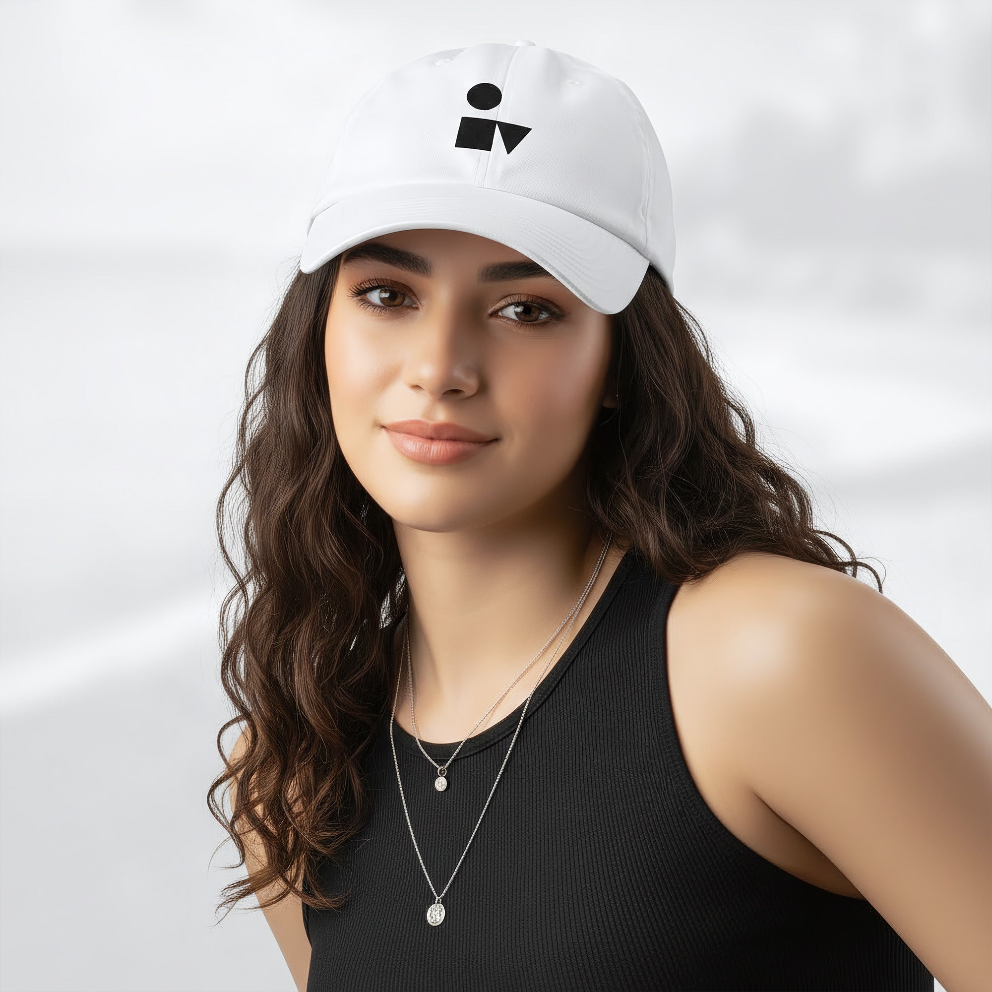 Female model wearing the white Under Armour x Form Fundamentals Stamp Cap (No.05); front view of the cap with black geometric emblem and curved brim, paired with a black tank top and layered necklaces against a softly blurred background.