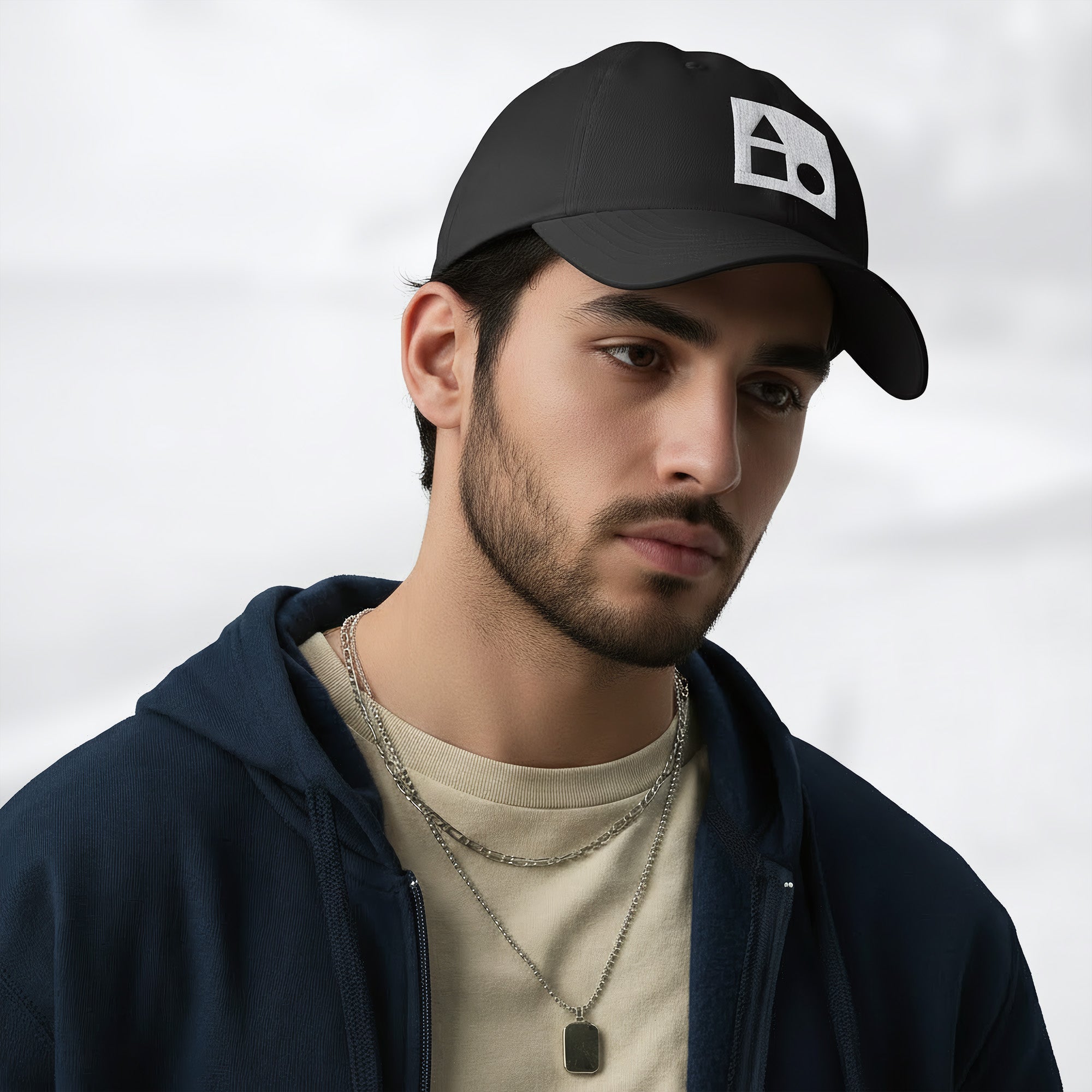 Male model wearing the black Under Armour x Form Fundamentals Stamp Cap (No.18) in a three‑quarter front pose; the cap’s curved brim and white Form Fundamentals logo are visible, styled with a navy hoodie over a beige top and layered chain in a neutral studio setting.