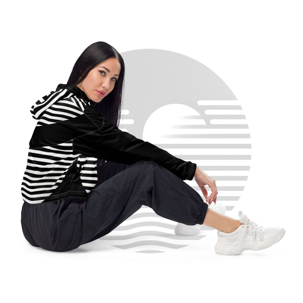 Side seated pose in white colourway ICN Cropped Windbreaker—striped sleeve detail and shoulder panel visible, cropped fit, styled with black joggers and white trainers from Form Finding Design.