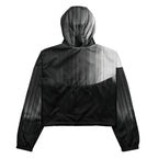 Back studio view of the HER Cropped Dither Distortion Windbreaker (No.10), showing the hood and cropped silhouette. The digital distortion print runs from light grey at the upper back to deep charcoal at the hem; the hood’s outer panels are colour‑blocked in black and white, and the elasticated hem is cinched with a drawcord, all set against a clean white backdrop